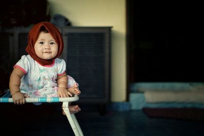 Portrait of cute baby girl sitting on bed