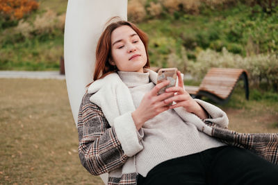 Young woman using mobile phone while sitting at park