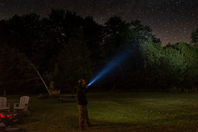 Man holding illuminated flashlight while standing in forest at night