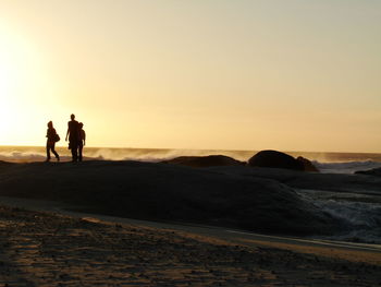 Silhouette people on beach against sky during sunset