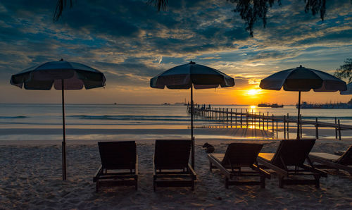 Deck chairs on beach against sky during sunset