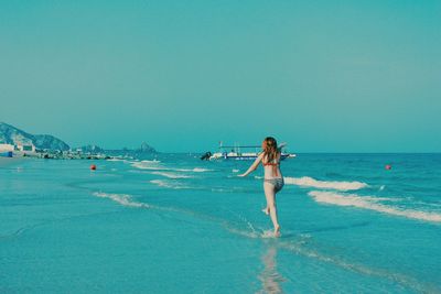 Full length of woman standing on beach against clear blue sky