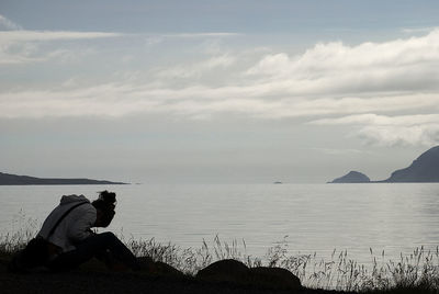 Man sitting on rock by sea against sky