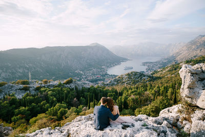 Rear view of woman sitting on rock against mountains