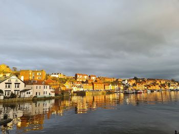 Buildings by river against sky in city