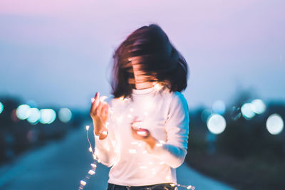 Close-up of young woman standing against illuminated sky