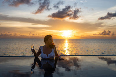 Attractive woman on a infinity pool near the ocean with a glass of champagne