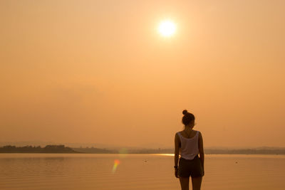 Rear view of woman standing at beach during sunset