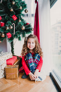 Portrait of smiling girl sitting by christmas tree