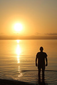 Silhouette man standing on shore at beach against sky during sunset