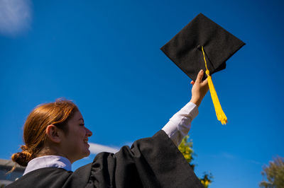 Side view of friends holding mortarboard against sky