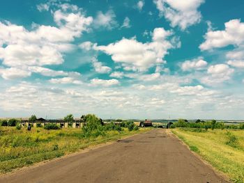 Road passing through field against cloudy sky