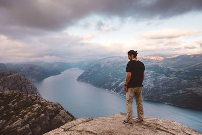 Man standing on rock looking at mountains against sky