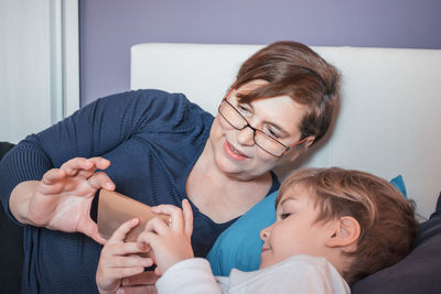 Grandmother and grandson looking at mobile phone while on bed at home