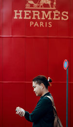 Side view of young man standing against red wall