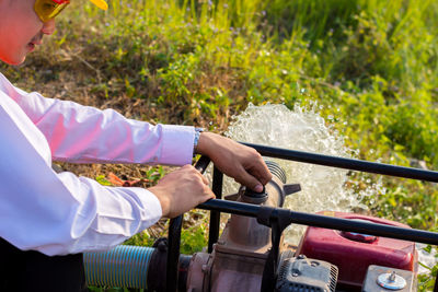 Cropped image of man holding pump spraying water at farm