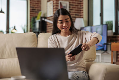 Smiling woman playing mobile game sitting on sofa at home