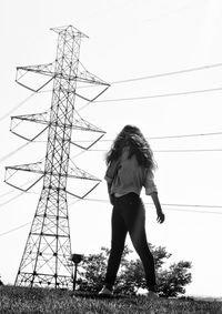 Full length of woman standing by electricity pylon on field