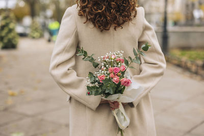 Young woman holding bouquet of flowers at footpath