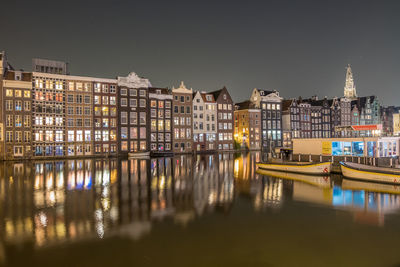 Illuminated buildings by river against sky at night