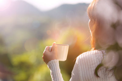 Close-up of hand holding coffee cup against sky