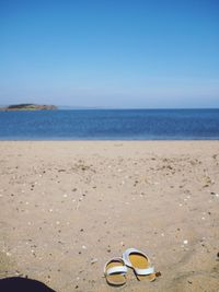 Close-up of shoes on beach against clear blue sky