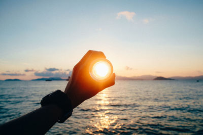 Close-up of woman hand holding sea against sky during sunset