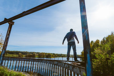 Rear view of man standing on railing against sky
