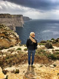 Woman standing on rock by sea against sky