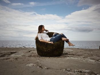 Rear view of woman sitting on beach against sky