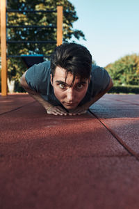 Young man doing push-ups on a red rubber ground during his workout