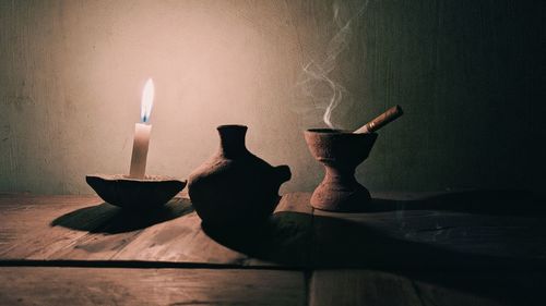 Close-up of hand holding lit candle on table