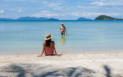 Rear view of woman standing at beach against sky