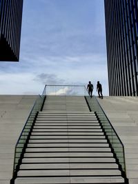 People walking on staircase of modern building against sky