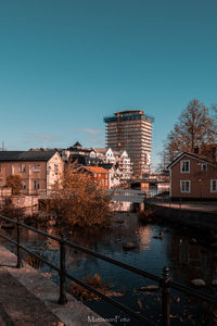 Buildings by river against clear blue sky