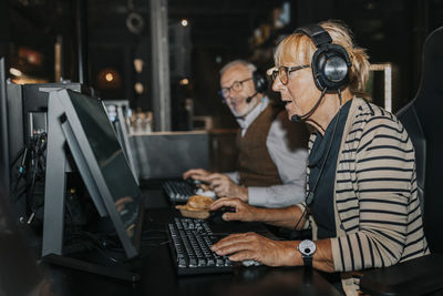 Senior woman playing video game on computer by male friend at gaming center