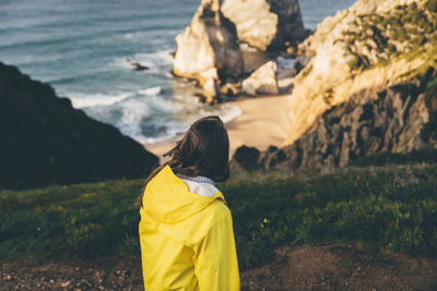 Rear view of woman wearing yellow raincoat looking at sea