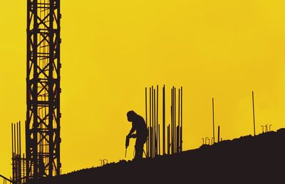 Silhouette man working at construction site against sky during sunset