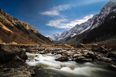 Stream flowing by mountains against sky