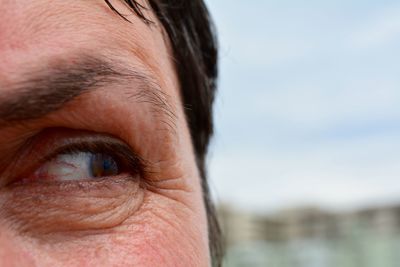 Cropped image of woman eye against sky