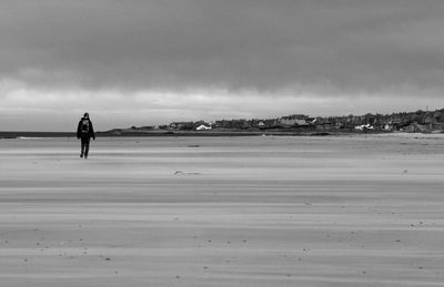 Man walking on beach against sky