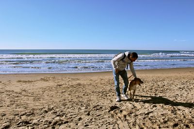 Man with dog on beach against clear sky