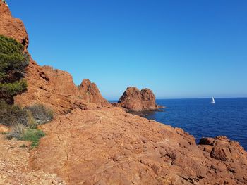 Scenic view of cliff by sea against clear blue sky