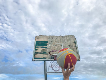 Cropped hand of person making basket against cloudy sky