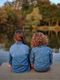 Rear view of siblings sitting on jetty over lake against trees