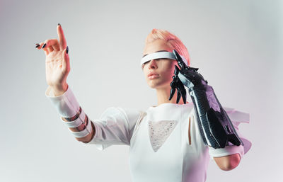 Portrait of young woman with arms raised standing against sky