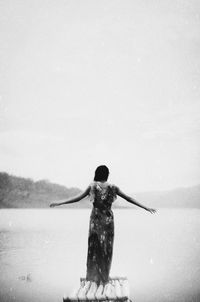 Rear view of woman with arms outstretched standing on shore