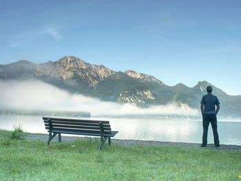 Man sit lone on a bench in park next lake. mountain range with amazing view over smooth lake surface