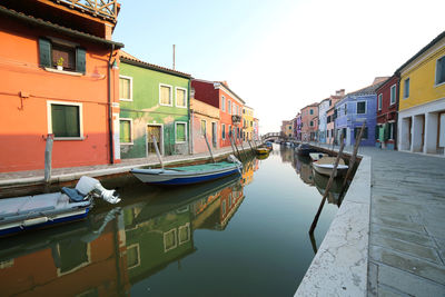 Boats moored on canal in city against sky