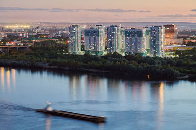 Illuminated buildings by river against sky in city